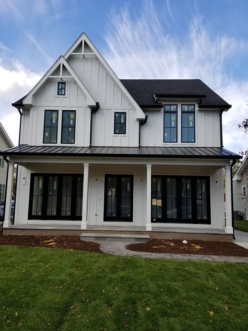 White house with vertical siding, black windows, and a covered front porch